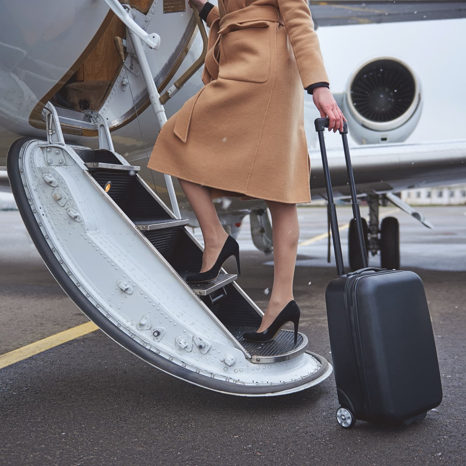 A traveler with a suitcase beside aircraft boarding stairs